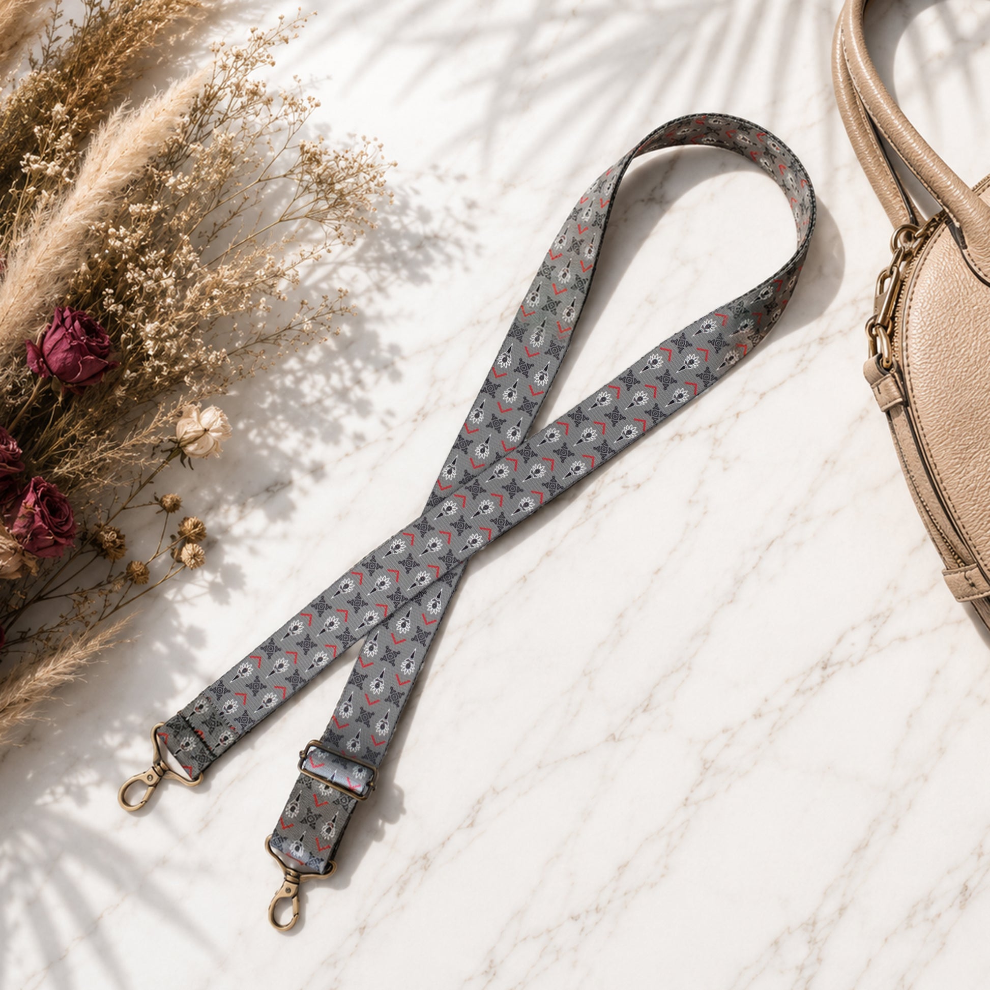 Floral patterned strap with gold hardware on a light surface with dried flowers and a beige bag.