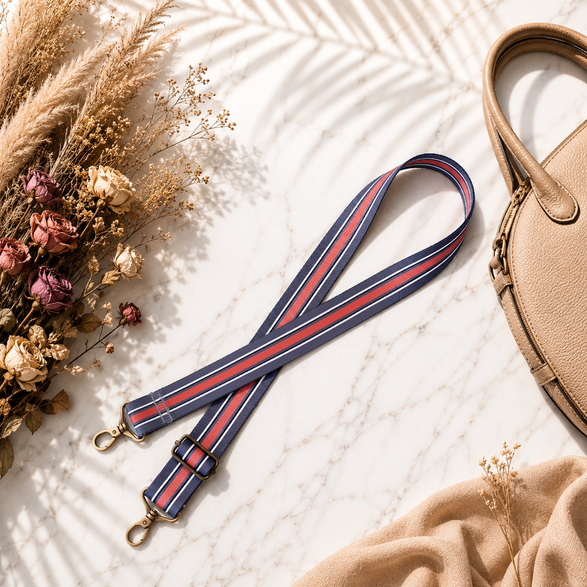 Striped bag strap with a beige handbag and dried flowers on a textured surface