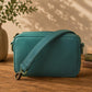 Emerald crossbody bag on a wooden surface with a plant and books in the background