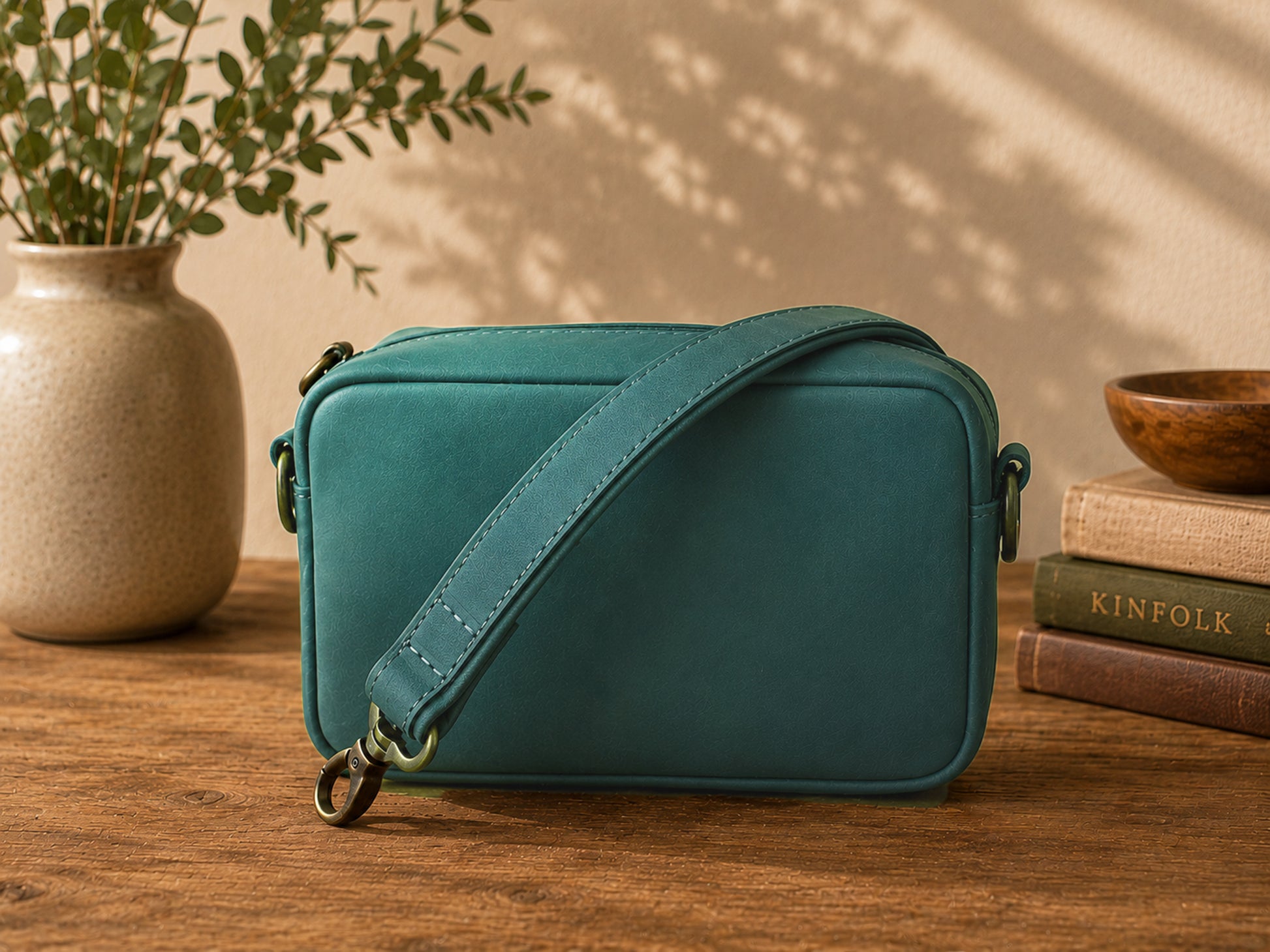 Emerald crossbody bag on a wooden surface with a plant and books in the background