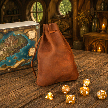A brown leather drawstring bag stands on a rustic wooden table, with several translucent gold polyhedral dice scattered in front. A fantasy map box is visible in the background against a warm, dimly lit medieval-style interior.