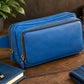 Blue leather crossbody on a wooden surface with a plant and Chanel perfume bottle in the background