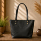 Black leather tote bag on a wooden surface with decorative plants and vases in the background.