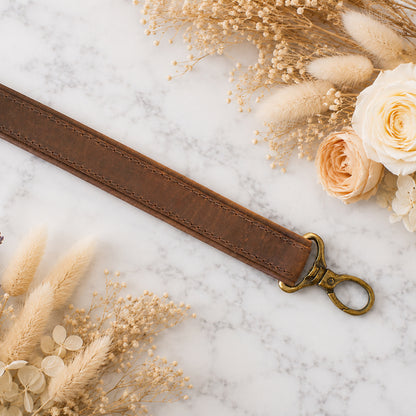 Brown leather strap with gold clasp on a marble surface with flowers