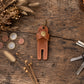 A brown leather golf ball divider keychain with a brass snap button, displayed on a rustic wooden tabletop with keys, coins, and dried grasses.