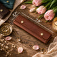 A brown leather wallet or card holder laid on a rustic wooden surface with overlaid dimension lines showing 2.7" by 7.
