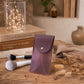 A small leather pouch or case with a flap closure and a single metal snap, standing upright on a wooden surface. The pouch has a muted plum-brown color.