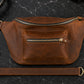 Brown leather waist bag with gold zippers on a dark marble surface.