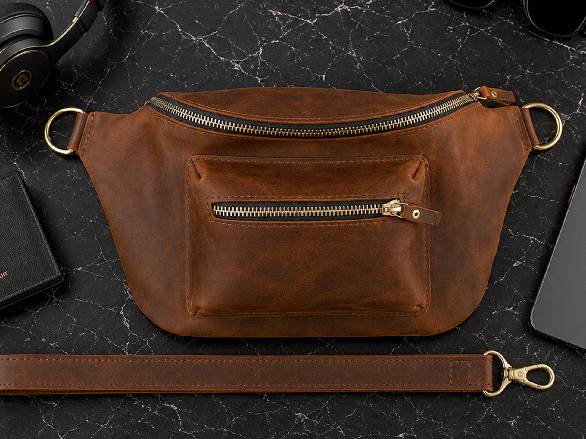 Brown leather waist bag with gold zippers on a dark marble surface.