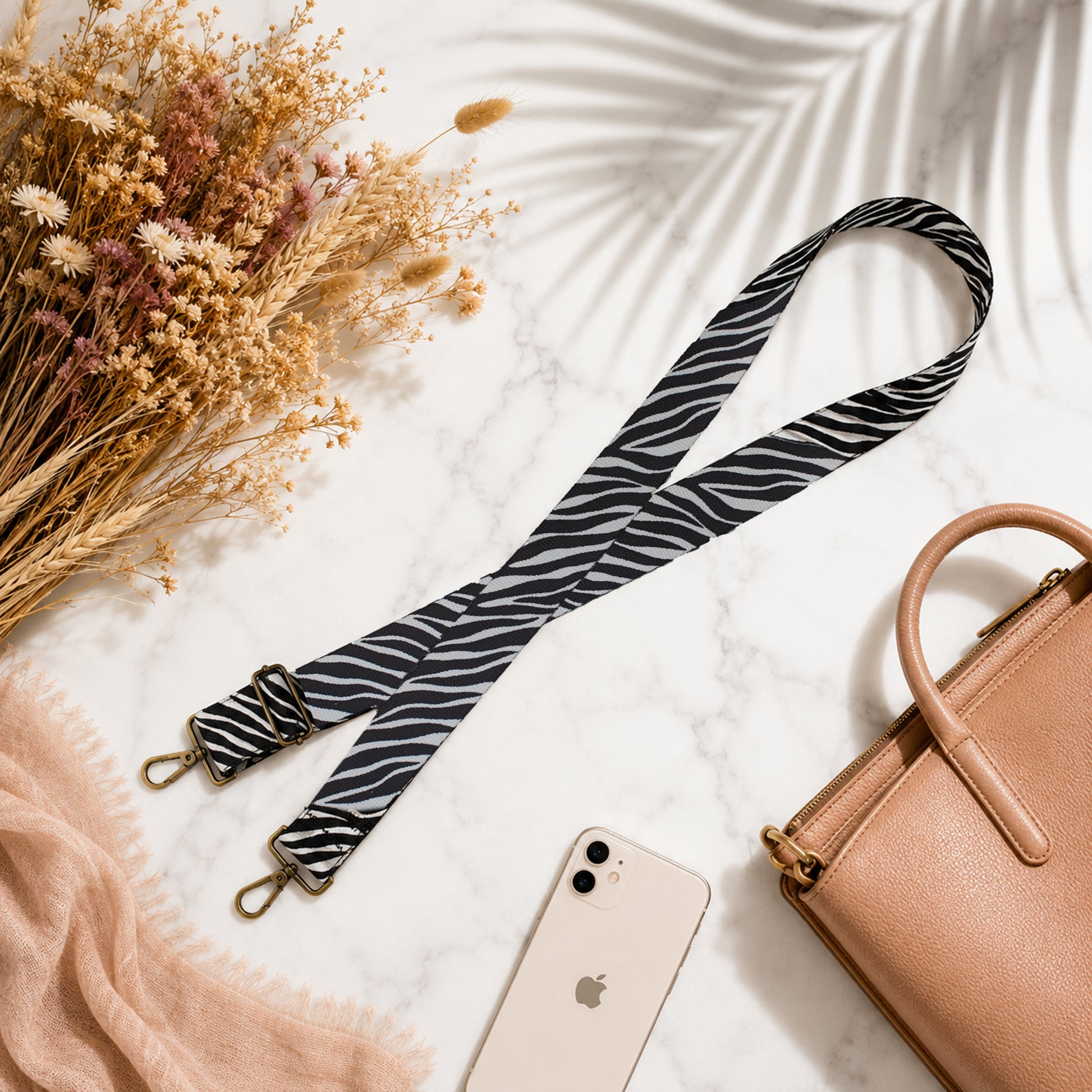 Zebra patterned strap with a phone, beige handbag, and dried flowers on a light background