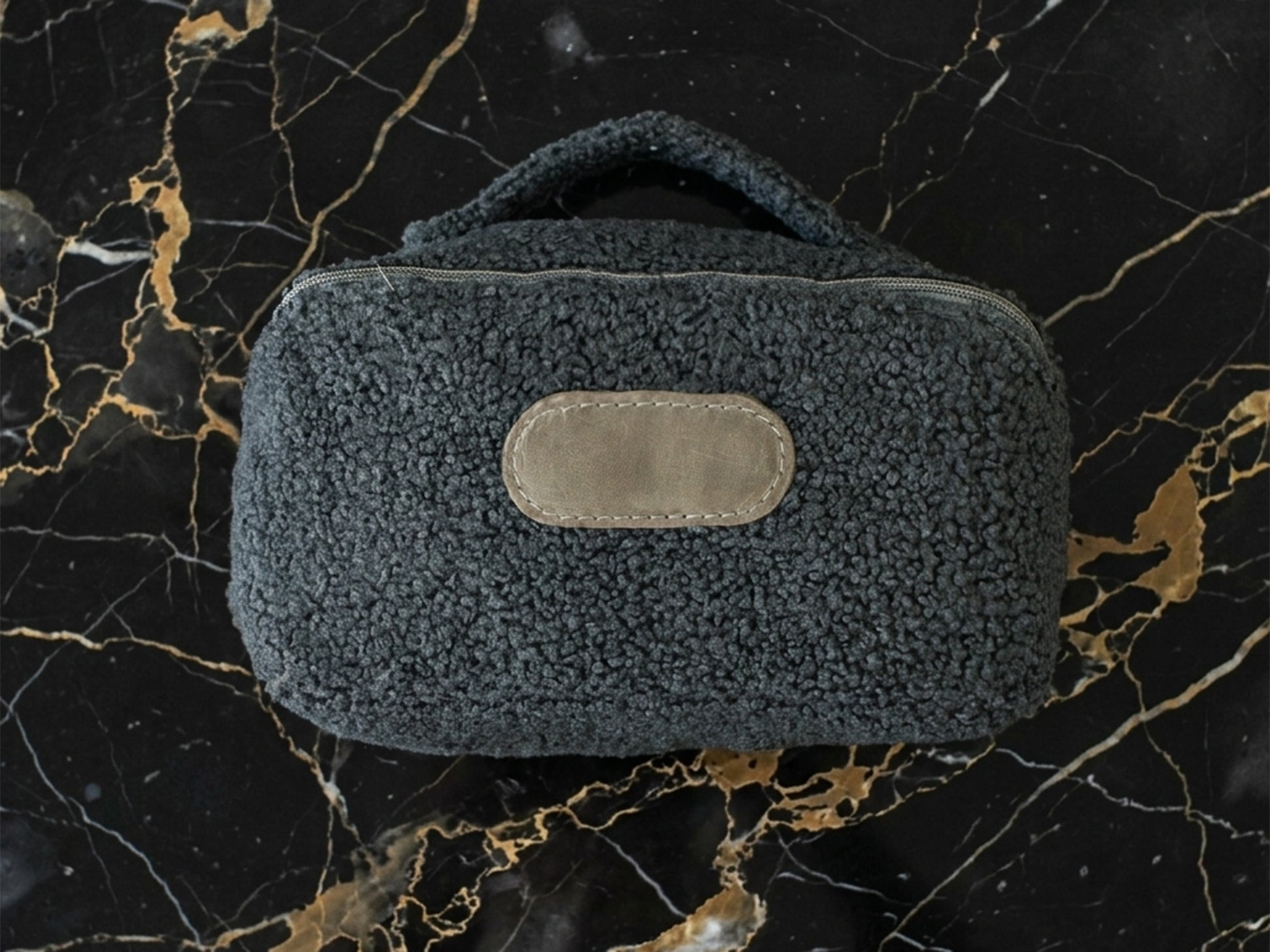 Dark gray textured pouch with a brown patch on a black marble background