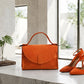 Orange handbag and high heels on a marble surface with a blurred outdoor background