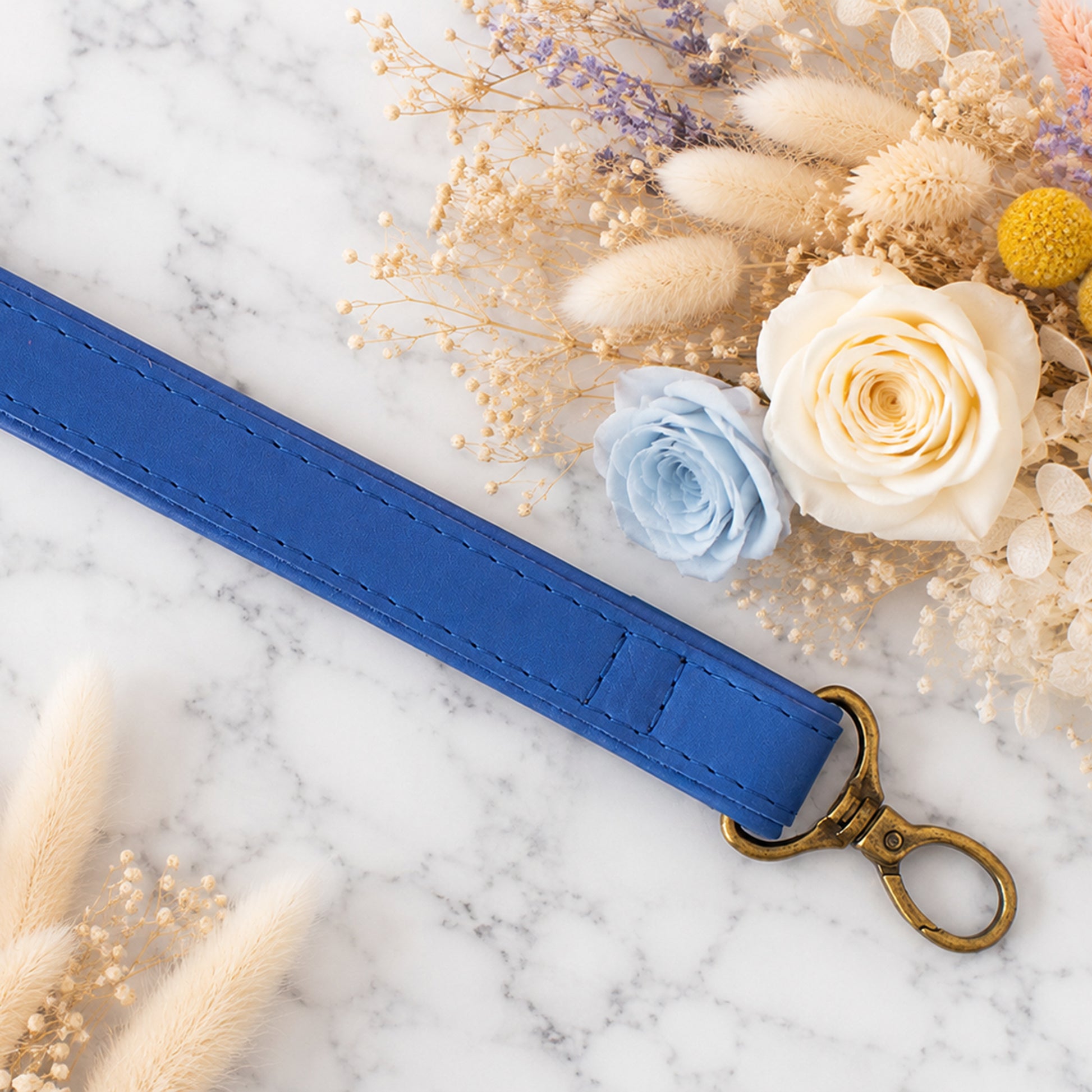 Blue strap with a gold clasp on a marble surface with flowers