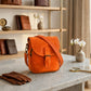 Orange leather bag on a marble surface with decorative items in the background