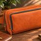 Orange leather crossbody bag on a wooden surface with a plant in the background