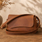 Brown leather bag on a wooden surface with a vase of dried flowers in the background