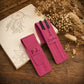 Two pink leather pen cases on a rustic wooden table, styled with an open sketchbook and dried flowers. One case is personalized with 'P.