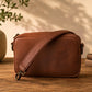 Brown leather crossbody bag on a wooden surface with a neutral background