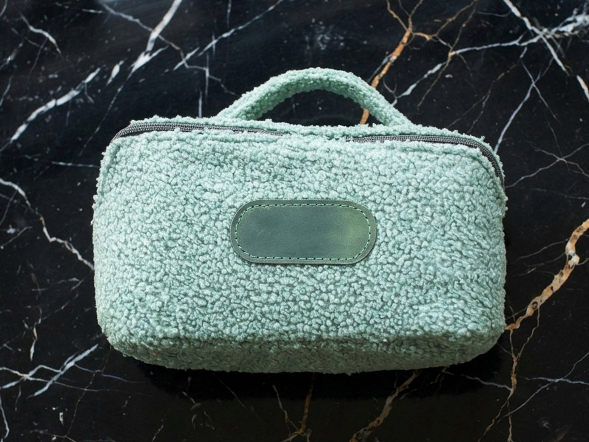 Green textured handbag on a black marble surface