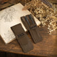 Two dark brown leather pen holders on a wooden table, one labeled 'JACK' and one labeled 'Lucas', styled with an open sketchbook and dried flowers.