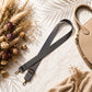 Black polka dot bag strap with gold hardware on a textured surface with dried flowers and a beige handbag.