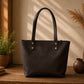 Black leather tote bag on a wooden surface with decorative plants and vases.