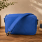 Blue crossbody bag on a wooden surface with books and a plant in the background