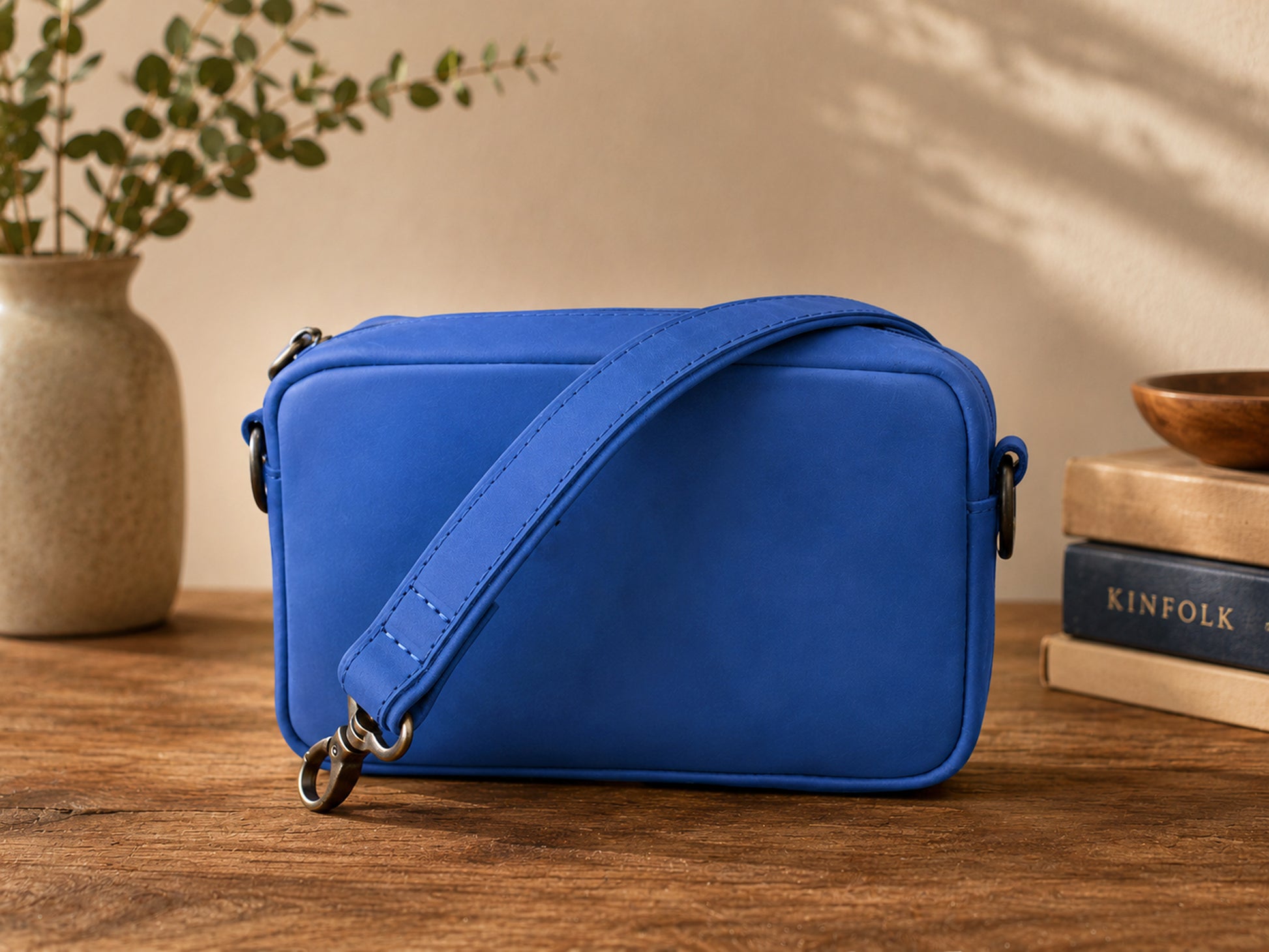 Blue crossbody bag on a wooden surface with books and a plant in the background