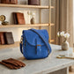 Blue satchel bag on a marble table with decorative items in the background
