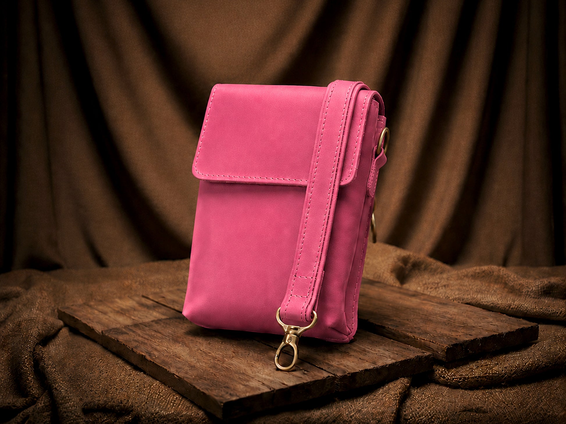Pink crossbody bag on a wooden surface with a brown fabric background