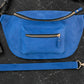 Blue waist bag with gold zippers on a black surface