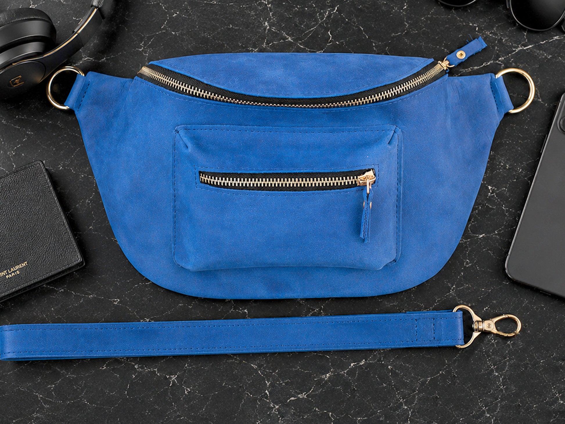 Blue waist bag with gold zippers on a black surface