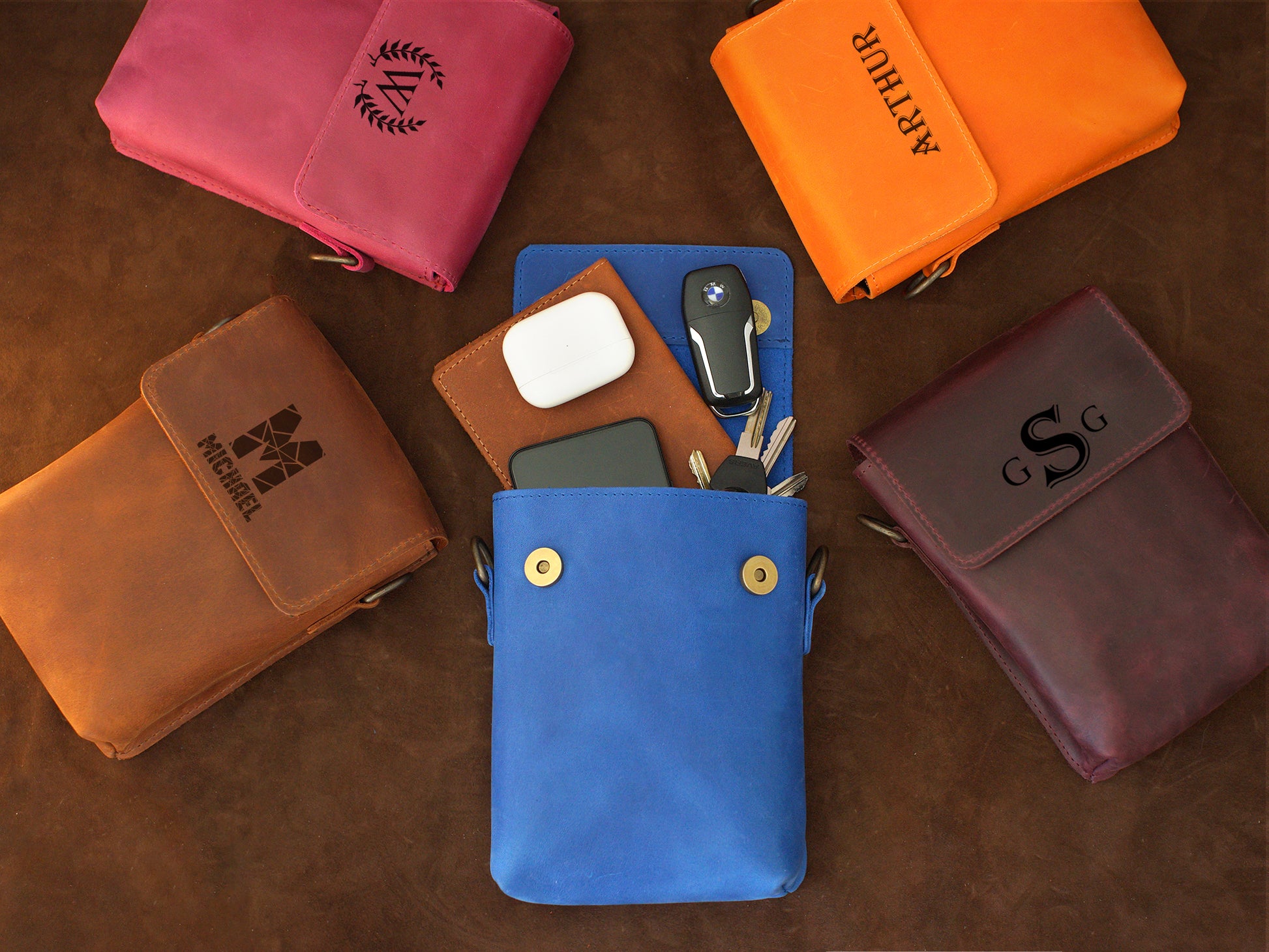 Collection of leather pouches in various colors with monogramming on a brown surface.