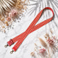 Red polka dot strap with gold hardware on a marble surface with dried flowers.