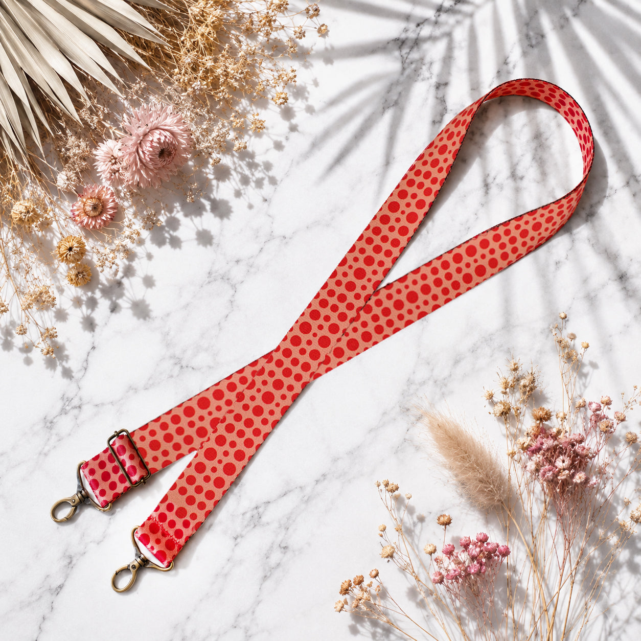 Red polka dot strap with gold hardware on a marble surface with dried flowers.