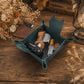 A teal blue felt car key holder tray filled with various keys, a watch, a perfume bottle, and coins, styled on a rustic wooden table with dried flowers and a vintage lantern.