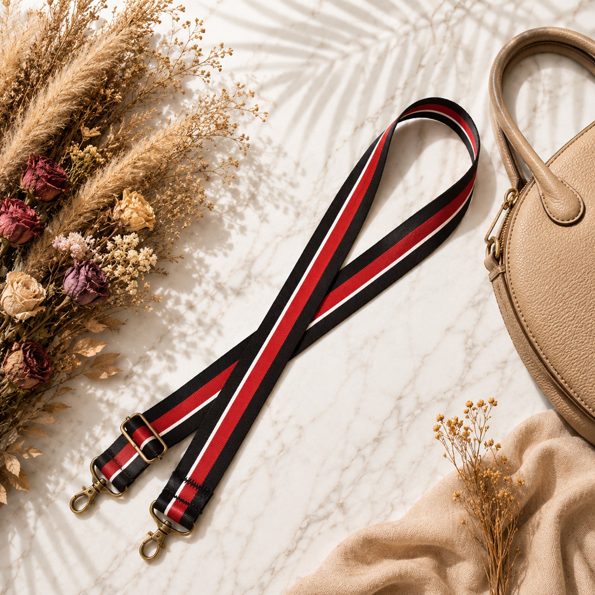 Strap with red and black stripes on a textured surface with dried flowers and a beige handbag.