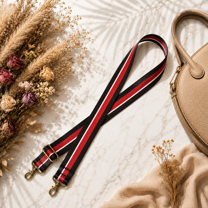 Strap with red and black stripes on a textured surface with dried flowers and a beige handbag.
