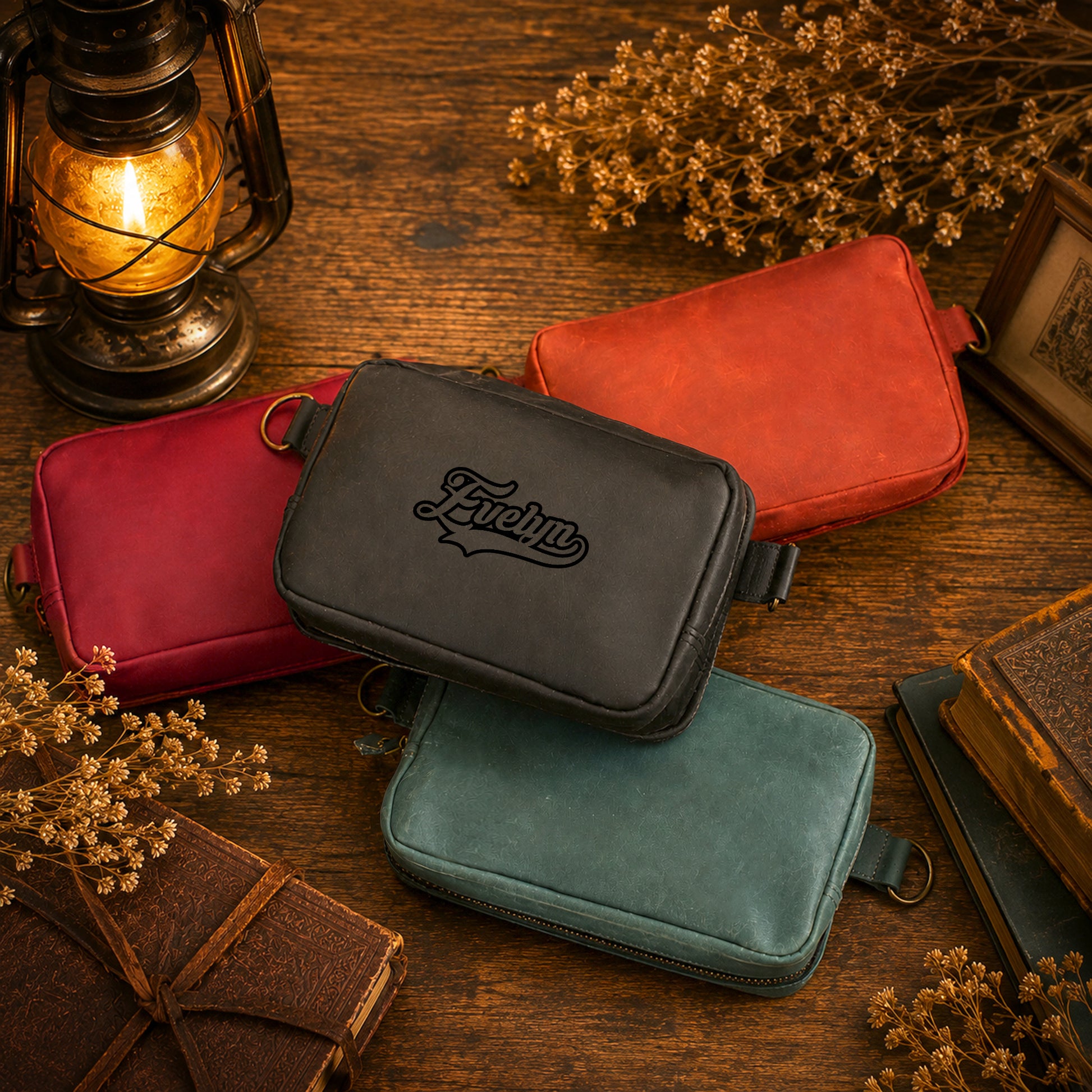 Four small zippered pouches or cases in red, black, teal, and rust orange are arranged on a rustic wooden table with vintage props including a lantern, books, and dried flowers. The black case in the center features an embossed script logo reading 'Echlin'.