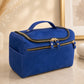 Blue cosmetic bag with gold zippers on a light wooden surface.