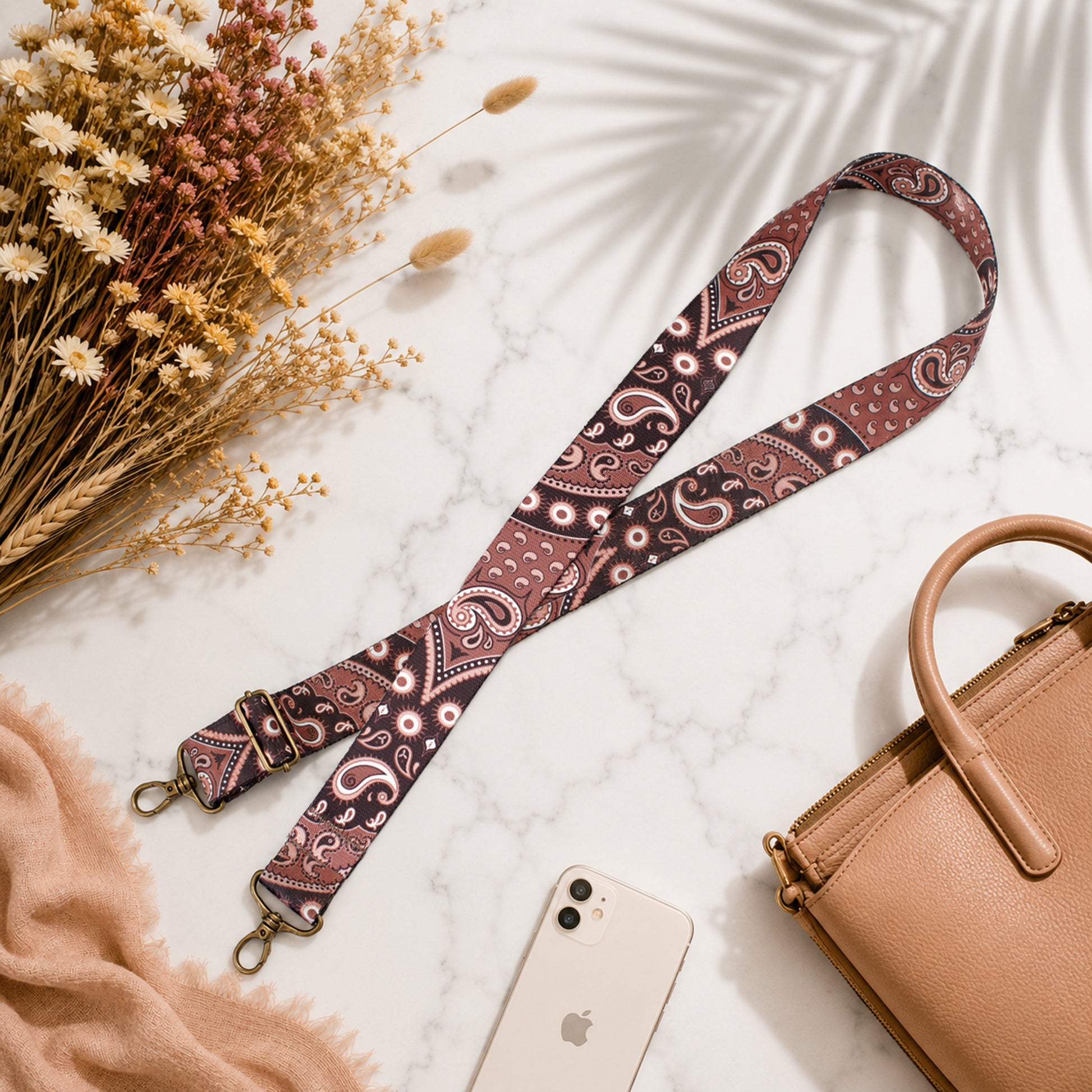 Patterned strap with a phone and handbag on a marble surface with flowers.