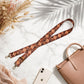 Plaid strap with gold hardware on a marble surface with a phone and handbag.