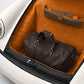 Brown leather duffel bag and suitcase in a car trunk with orange interior.