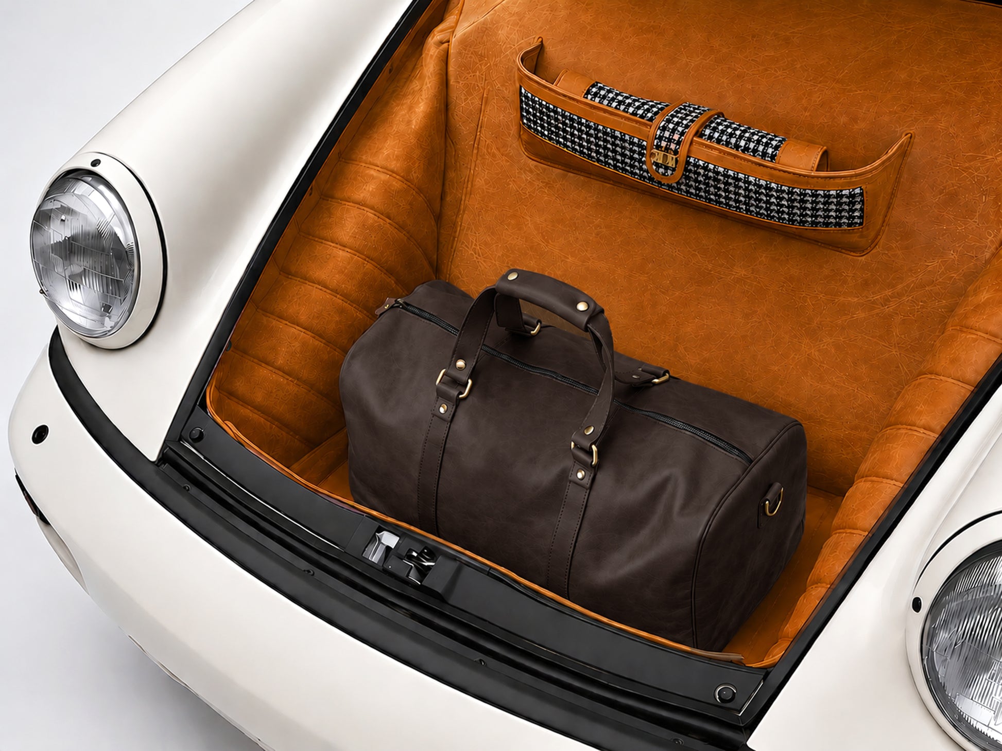 Brown leather duffel bag and suitcase in a car trunk with orange interior.