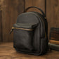 Small dark backpack with a gold zipper on a wooden surface.