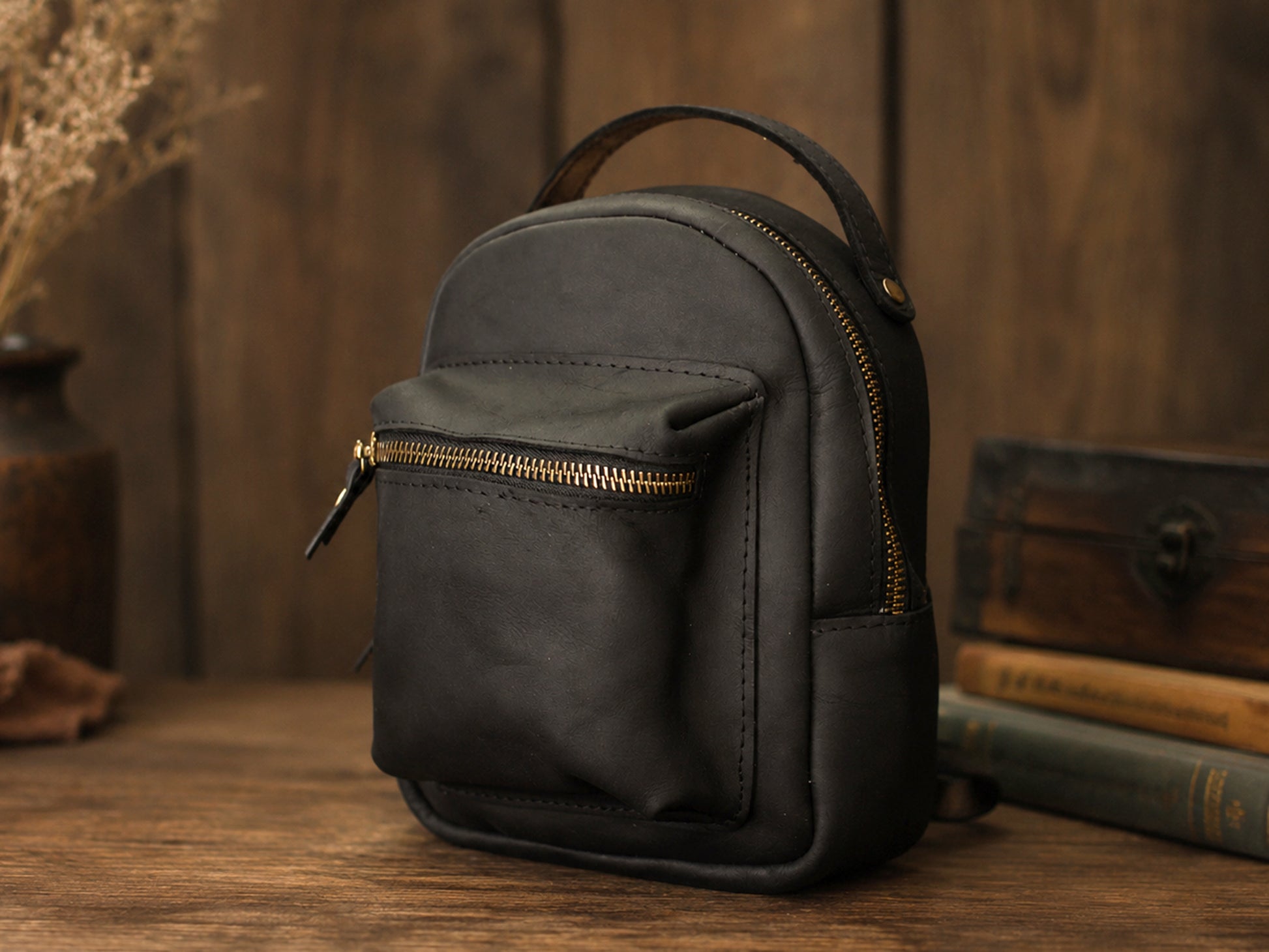 Small dark backpack with a gold zipper on a wooden surface.