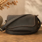 Brown leather bag on a wooden surface with a vase of dried flowers in the background