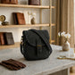 Black leather bag on a marble surface with shelves and decor in the background