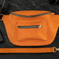 Orange crossbody bag on a dark surface with accessories around
