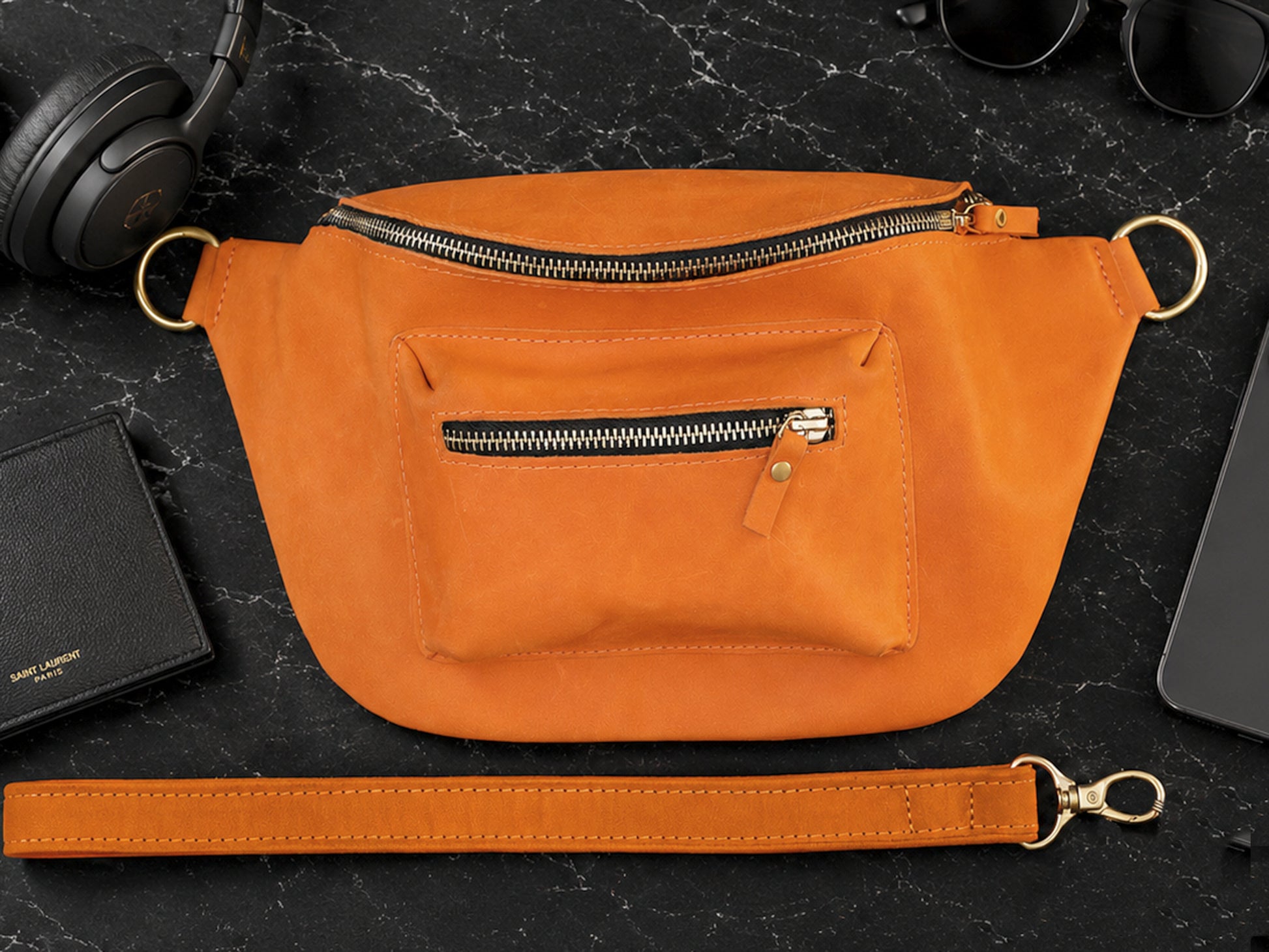 Orange crossbody bag on a dark surface with accessories around